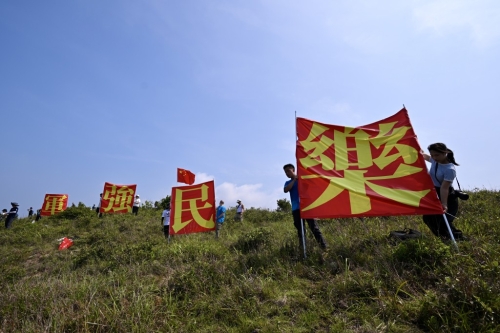 有市民于玉桂山顶上举起自制的“军强民乐”旗帜,表示是回应山东舰进港时甲板上的“国安家好”字句 。 有市民于玉桂山顶上举起自制的“军强民乐”旗帜,表示是回应山东舰进港时甲板上的“国安家好”字句 。