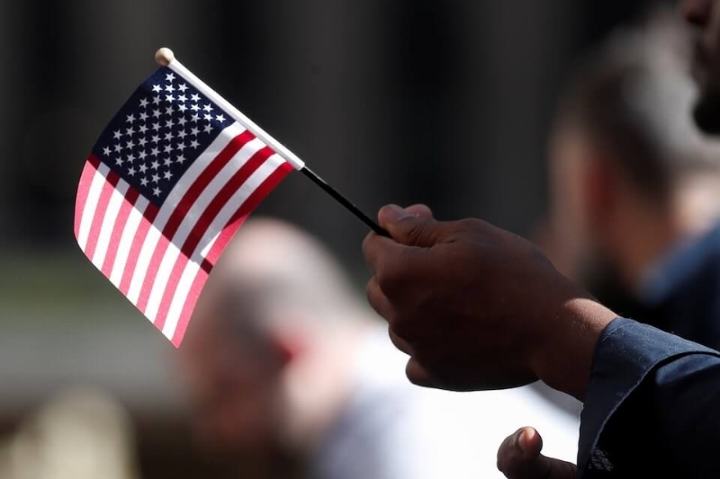 图为一名公民候选人在美国国籍暨移民局（USCIS）入籍仪式上挥舞国旗。